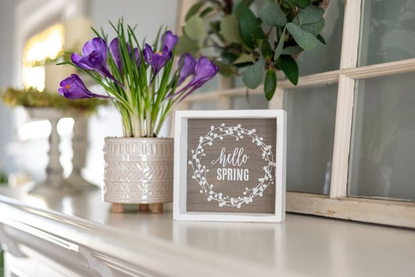Frühlingsdeko-Ideen: Hello spring Schild mit lila Blumen auf dem Kaminsims
